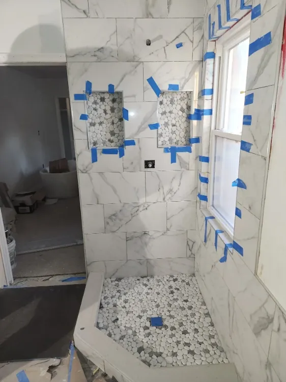 Shower view with white-and-gray veined wall tile, two pebble-mosaic niche backings, a window, and a light-and-dark rounded mosaic floor.